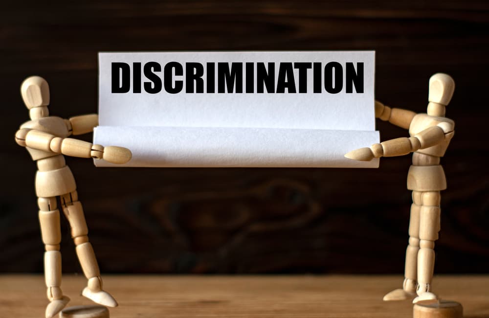 Two wooden men hold paper with the word DISCRIMINATION. Business concept.