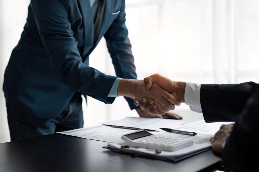 Business professionals or lawyers shaking hands after successful agreement or contract negotiation at office desk.