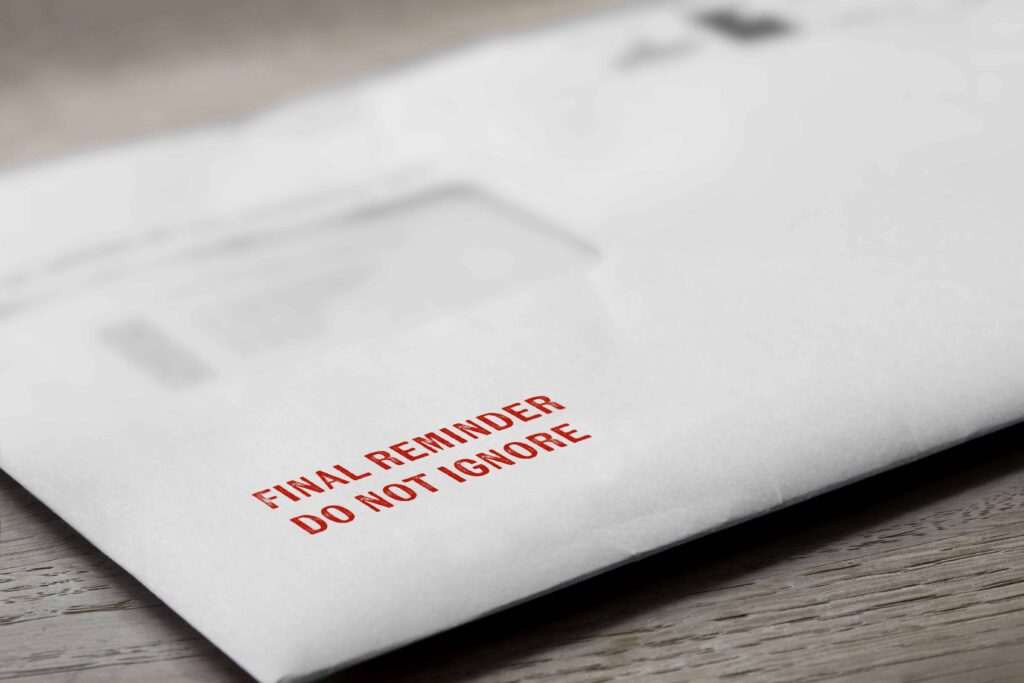 Final reminder letter envelope with red text warning &lsquo;Do Not Ignore&rsquo; on wooden desk.